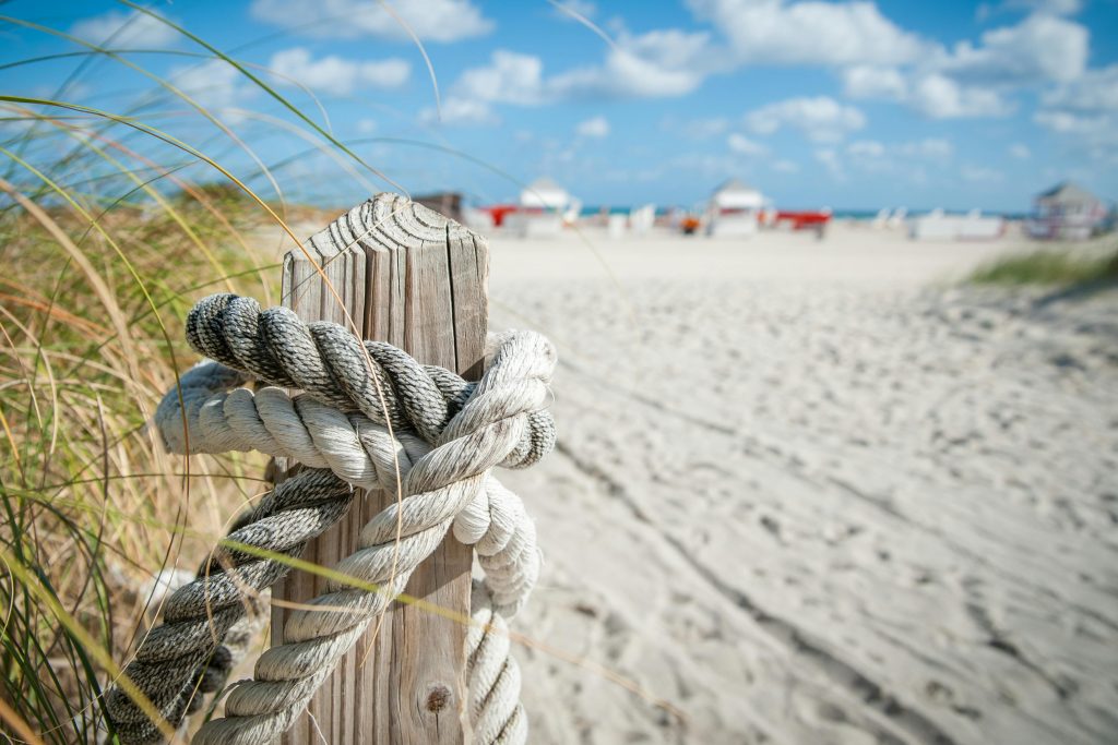 A detail shot of a rope tied around a wood post on a sandy beach.